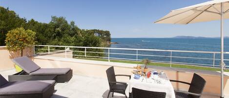 A terrace with wicker furniture, a table set for dining, and a view of the sea.