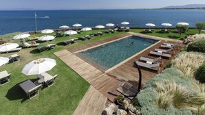 Un espace piscine avec des chaises longues et des parasols, une terrasse en bois et une vue sur la mer.
