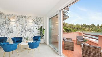 Een modern interieur met een marmeren wand, blauwe stoelen, een ronde tafel en een balkon met rieten meubels met uitzicht op een prachtig landschap.