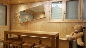 Interior de madeira com uma mesa grande e bancos, um urso de pelúcia e um espelho na parede.