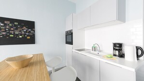 A modern kitchen with white cabinets, a black coffee maker, and a wooden table. - Primeflats - Apartment Weissensee (Berlin)