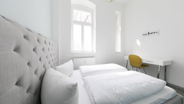A modern bedroom with a large bed, a desk, and a chair. - Primeflats - Apartment Weissensee (Berlin)