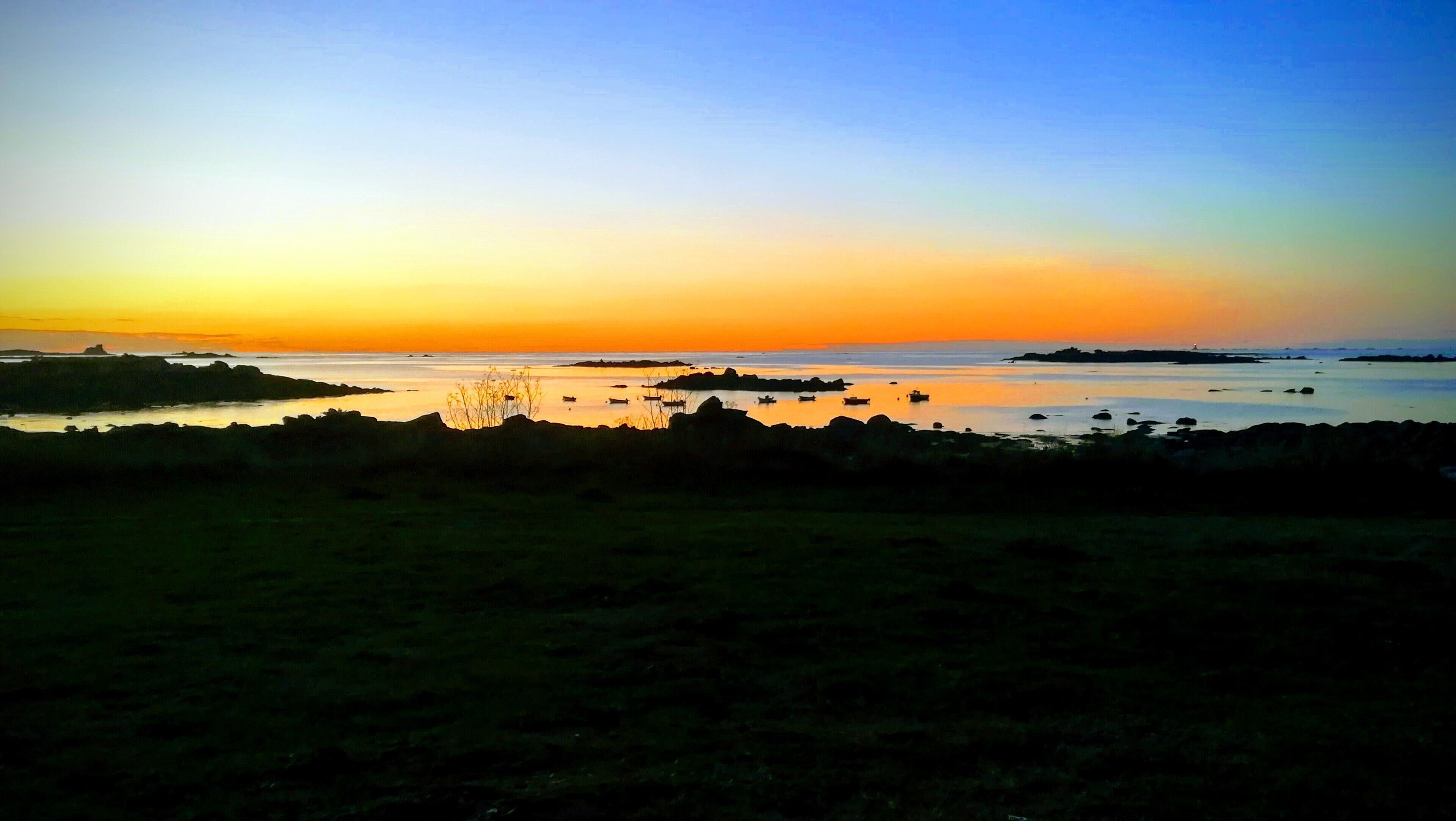 Un paisaje costero con atardecer, agua tranquila y barcos.