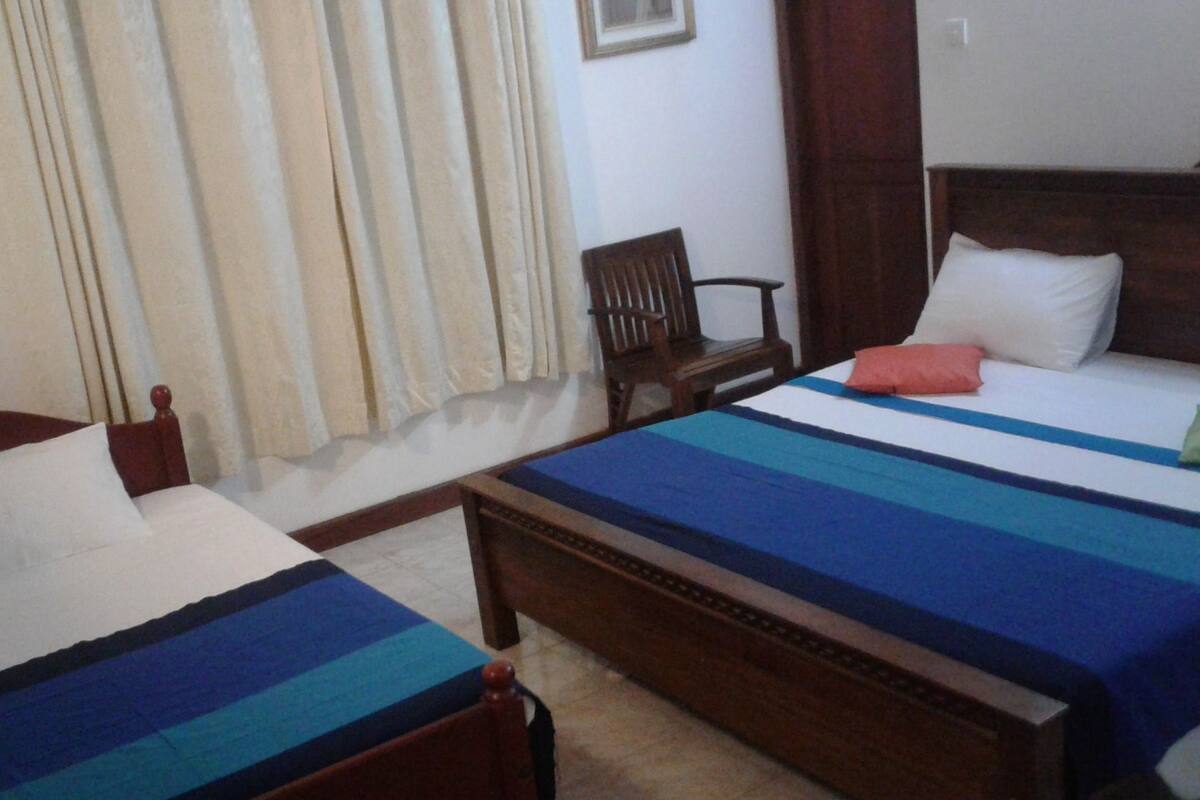 A hotel room with two single beds, a wooden headboard, a chair, and a window with curtains.