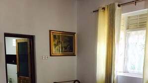 Habitació d'hotel amb un llit, una cadira de fusta, un quadre a la paret i una finestra amb cortines.