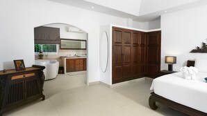 A bedroom with a large bed, a wooden wardrobe, a bathroom with a bathtub, and a kitchenette.