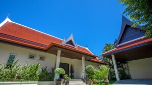 A traditional Thai house with a red tiled roof, a covered porch, and a well-maintained garden.
