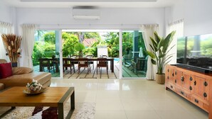 A spacious living room with a large TV, a sofa, a coffee table, and a dining area with chairs and a table.