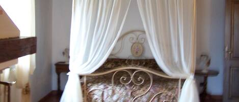 A four-poster canopy bed with white drapes, a wooden headboard, and a tiled floor.