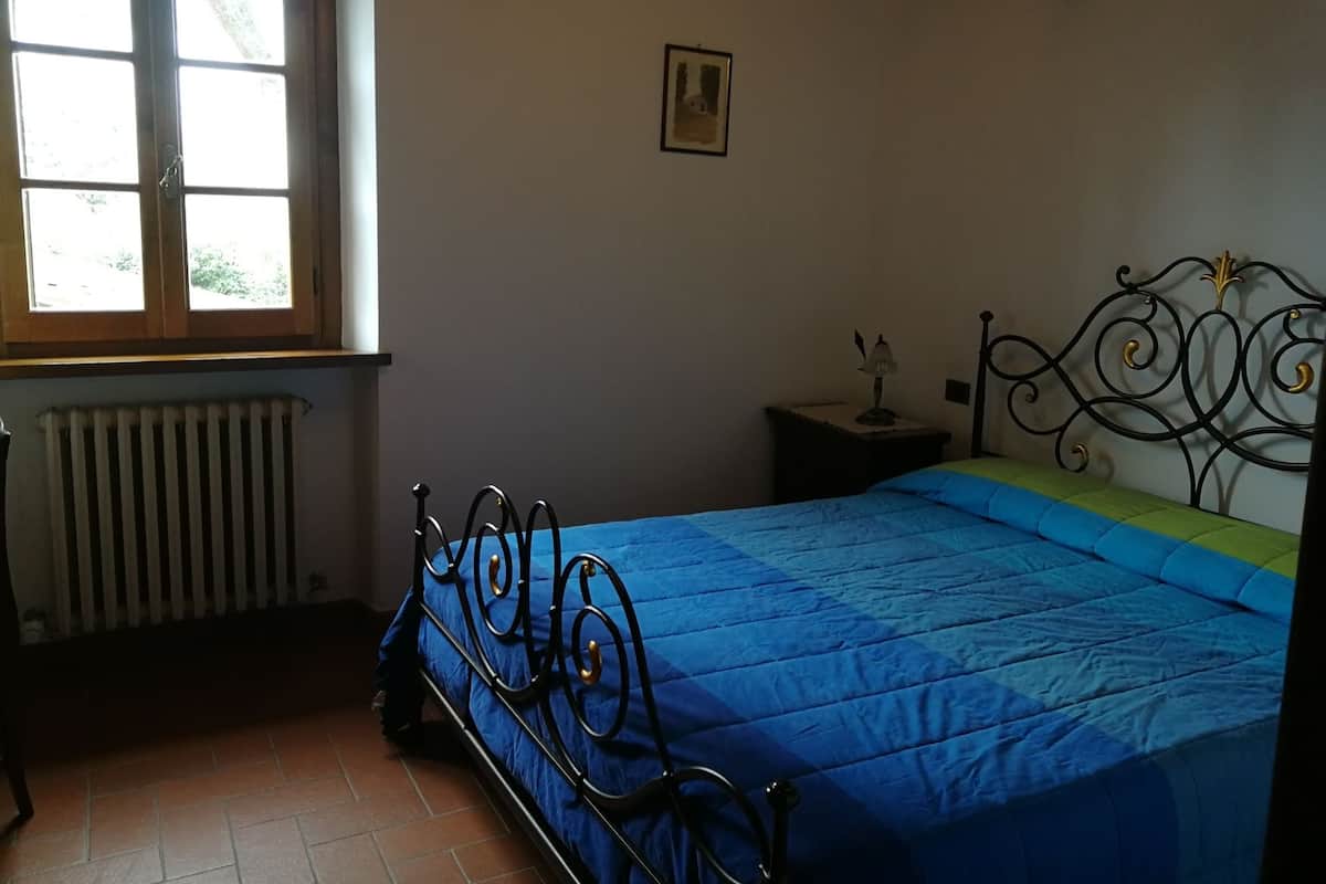 A bedroom with a bed, a radiator, a window, and a bedside table with a lamp.