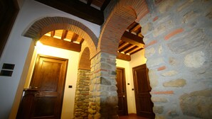 A hallway with stone columns, wooden doors, and a tiled floor. - B&B Ortali Country House (Arezzo)