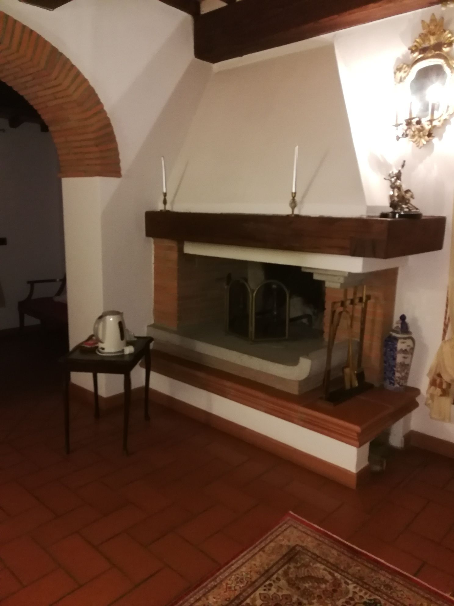 Une pièce chaleureuse avec une cheminée, une petite table avec une bouilloire et un tapis à motifs.