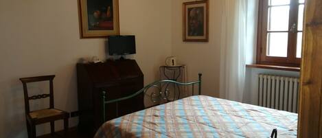 A bedroom with a bed, a chair, a desk with a computer, and two framed pictures on the wall.