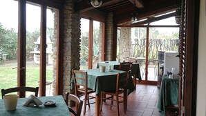 A covered patio with stone pillars, wooden tables, and chairs. - B&B Ortali Country House (Arezzo)