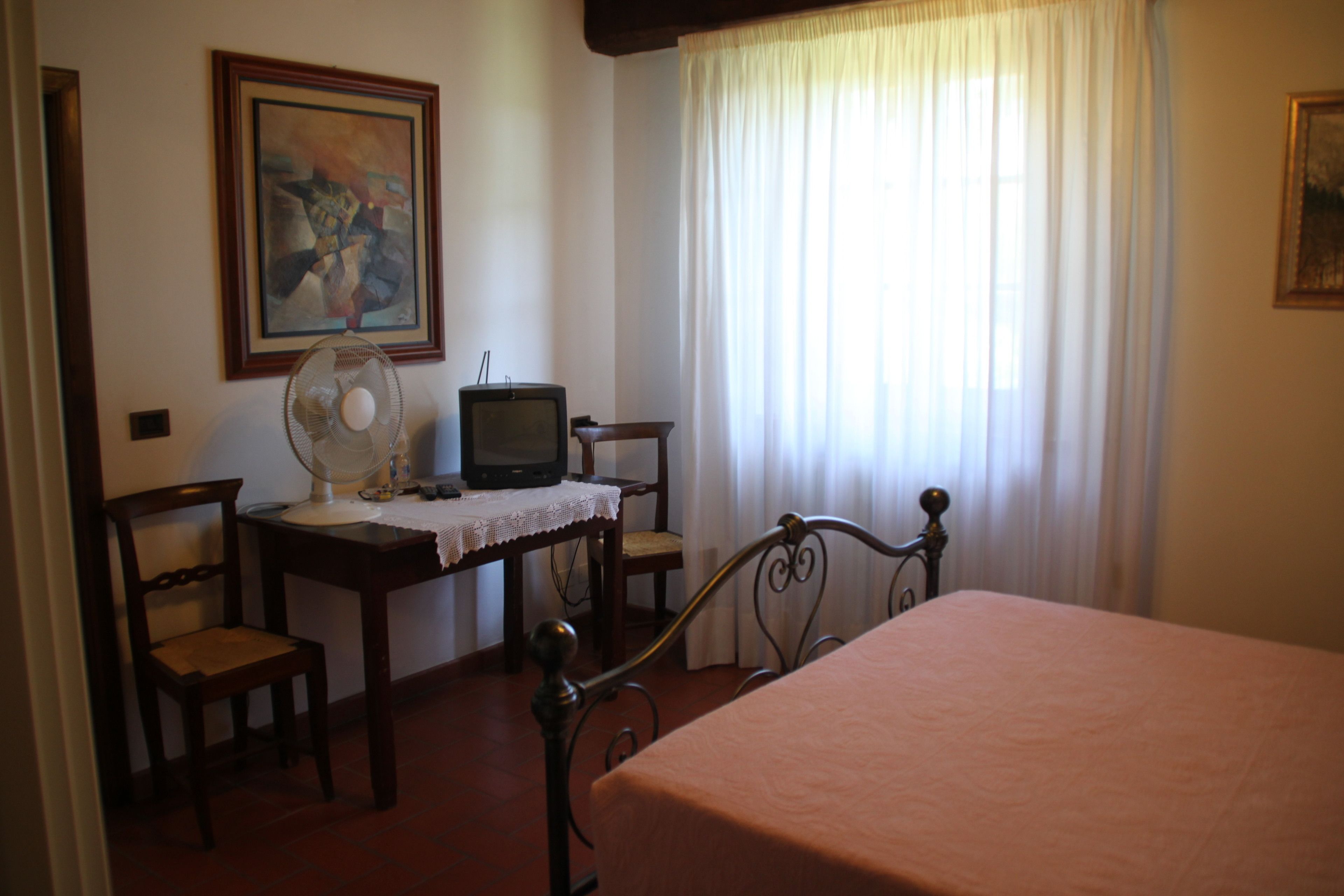 A bedroom with a bed, a desk with a television, a chair, and a fan.