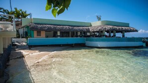 Un bâtiment situé en bord de mer, doté d’un toit de chaume, d’une piscine et d’une eau claire et peu profonde.
