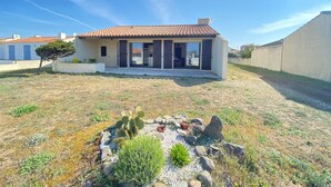Une maison de plain-pied avec un toit en tuiles, un patio couvert et un jardin agrémenté de cactus et d’arbustes.