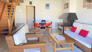 Un salon chaleureux avec des meubles en osier, un coin repas avec une nappe rouge et un escalier.