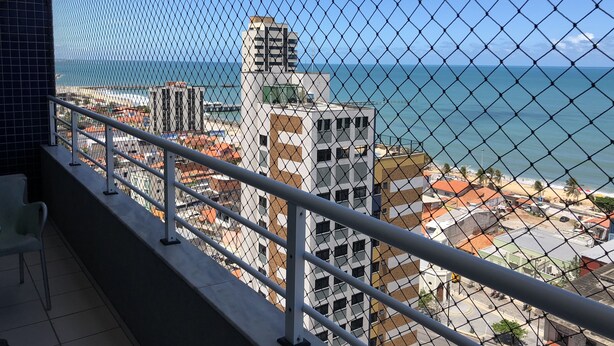 Un balcon doté d’une rambarde en treillis métallique, offrant une vue sur le paysage urbain de la côte, avec des bâtiments modernes et une vue dégagée sur l’océan.
