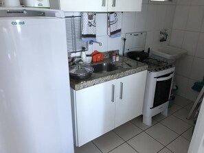 Ett kök med vita skåp, en bänkskiva i granit, en spis, ett diskho och ett kylskåp.