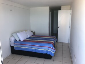 Ett litet, rent rum med en enkel säng, ett nattduksbord och en dörr som leder till ett annat rum.