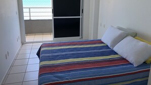 Une chambre avec un lit, une porte-fenêtre coulissante donnant sur un balcon et un climatiseur fixé au mur.