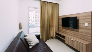Un salon moderne avec un canapé en cuir, un téléviseur à écran plat fixé sur un mur en bois et une grande fenêtre avec des rideaux.