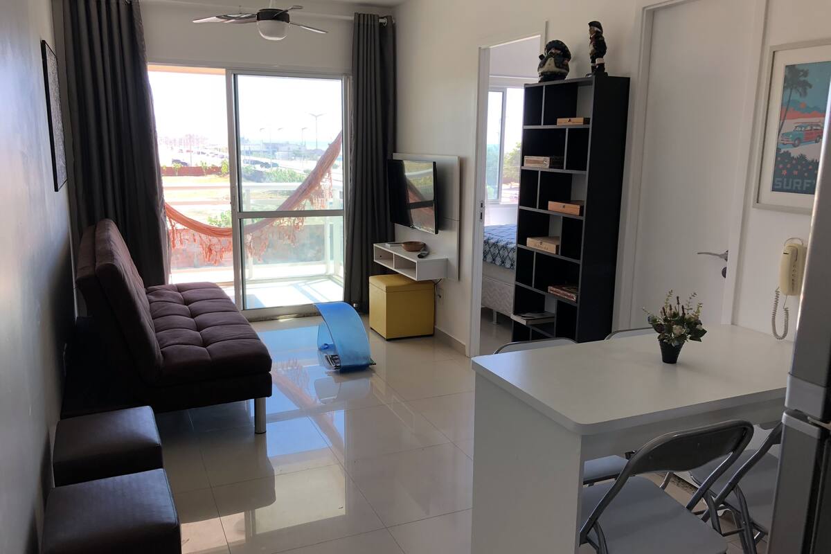 Sala moderna com sofá, televisão, estante de livros e varanda com vista.