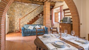 A dining area with a stone wall, wooden staircase, and a cozy blue sofa. - Tenuta La Pieve Casale La Valle (Pergine Valdarno)