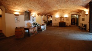 A spacious room with a high, vaulted ceiling and stone walls. There is a wooden barrel, a table with a vase of flowers, and several chairs arranged around a table. - Tenuta La Pieve Casale La Valle (Pergine Valdarno)