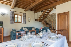 Uma sala de jantar com uma mesa posta para seis pessoas, escada, sofá e porta de madeira.
