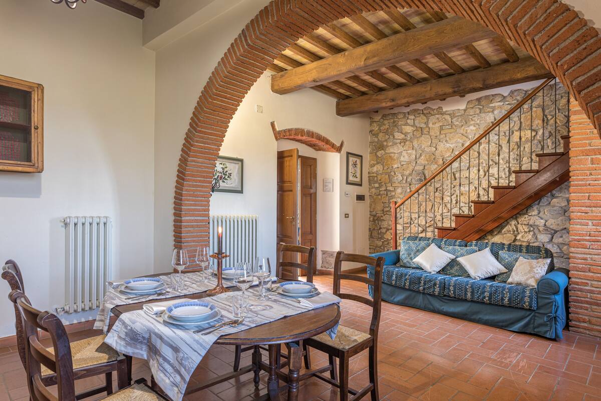 Un coin repas avec une table dressée pour quatre personnes, un mur en pierre et un escalier en bois.