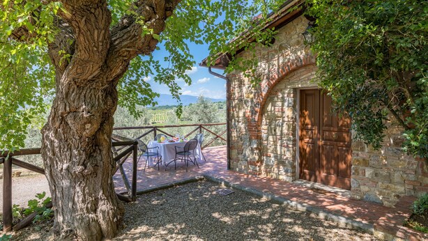 A rustic stone building with a wooden door, surrounded by greenery and a table with chairs outside. - Tenuta La Pieve Casale La Valle (Pergine Valdarno)