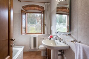 A bathroom with a bathtub, a sink, a toilet, and a window with a view of the outdoors. - Tenuta La Pieve Casale La Valle (Pergine Valdarno)