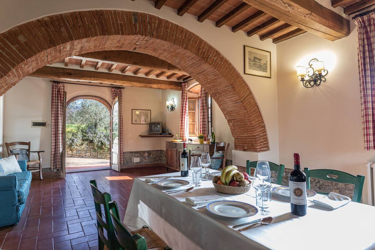 A dining area with a table set for two, a wine bottle, and a fruit basket.