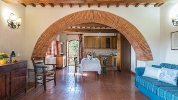 A spacious dining area with a brick archway, wooden ceiling beams, and a view into the kitchen.