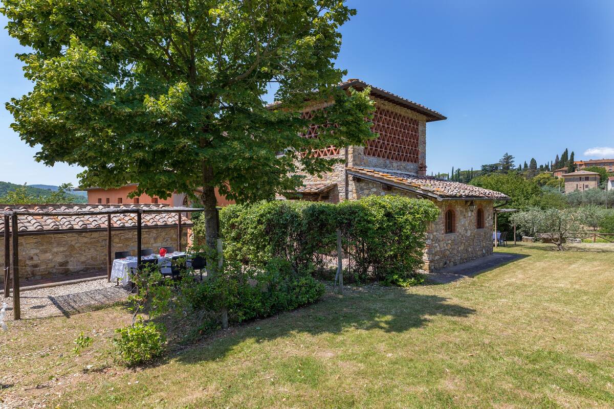 A stone building with a tiled roof, surrounded by a grassy area and trees.