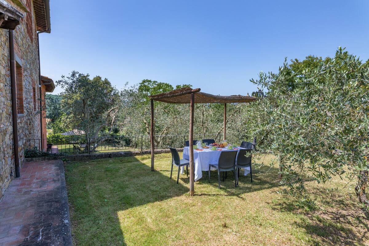 An outdoor dining area with a pergola, a table set with plates and glasses, and chairs.