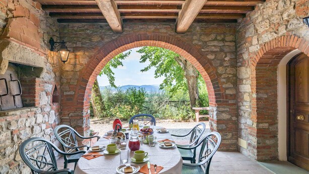 A stone archway with a table set for breakfast, overlooking a scenic landscape.