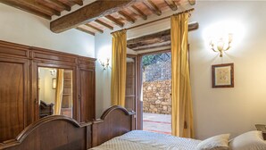 A bedroom with a wooden bed, a stone wall outside, and a chandelier.