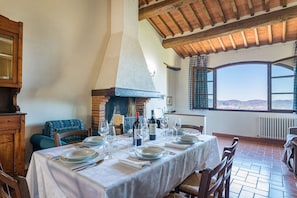 A dining room with a table set for a meal, a brick fireplace, and a view through large windows. - Tenuta La Pieve Casale Il Giglio (Pergine Valdarno)