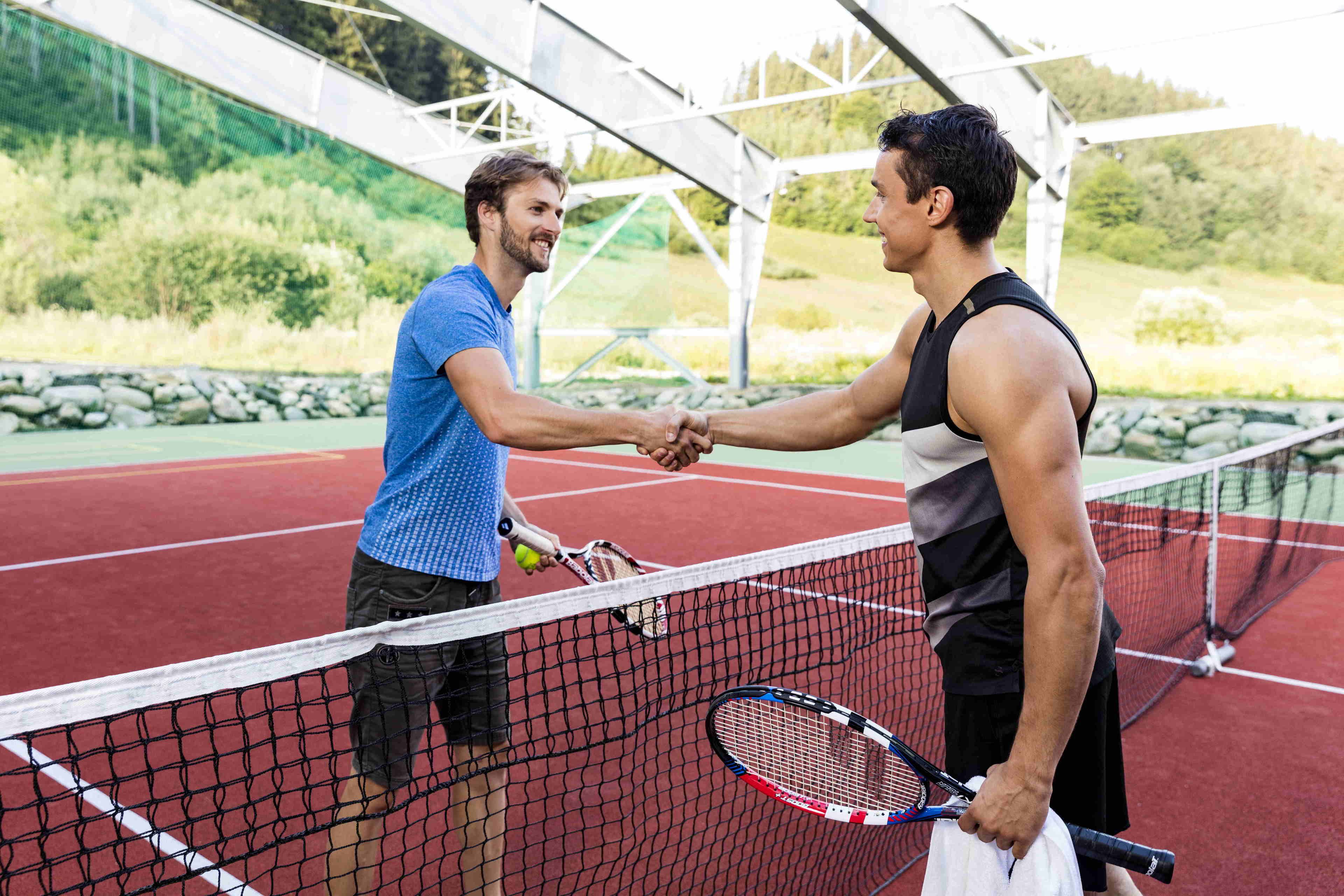 Two people shaking hands on a tennis court with a net in the middle.