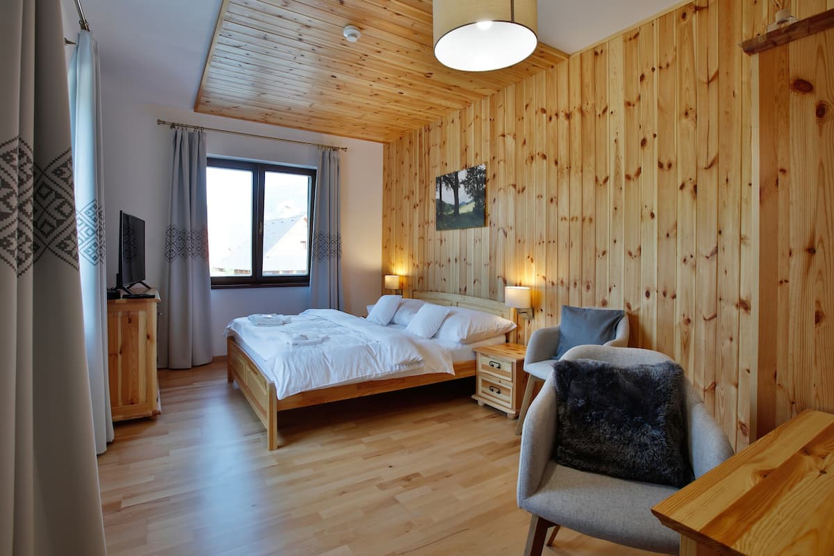 Una habitación con paneles de madera, una cama, mesitas de noche, una silla y un ventanal.