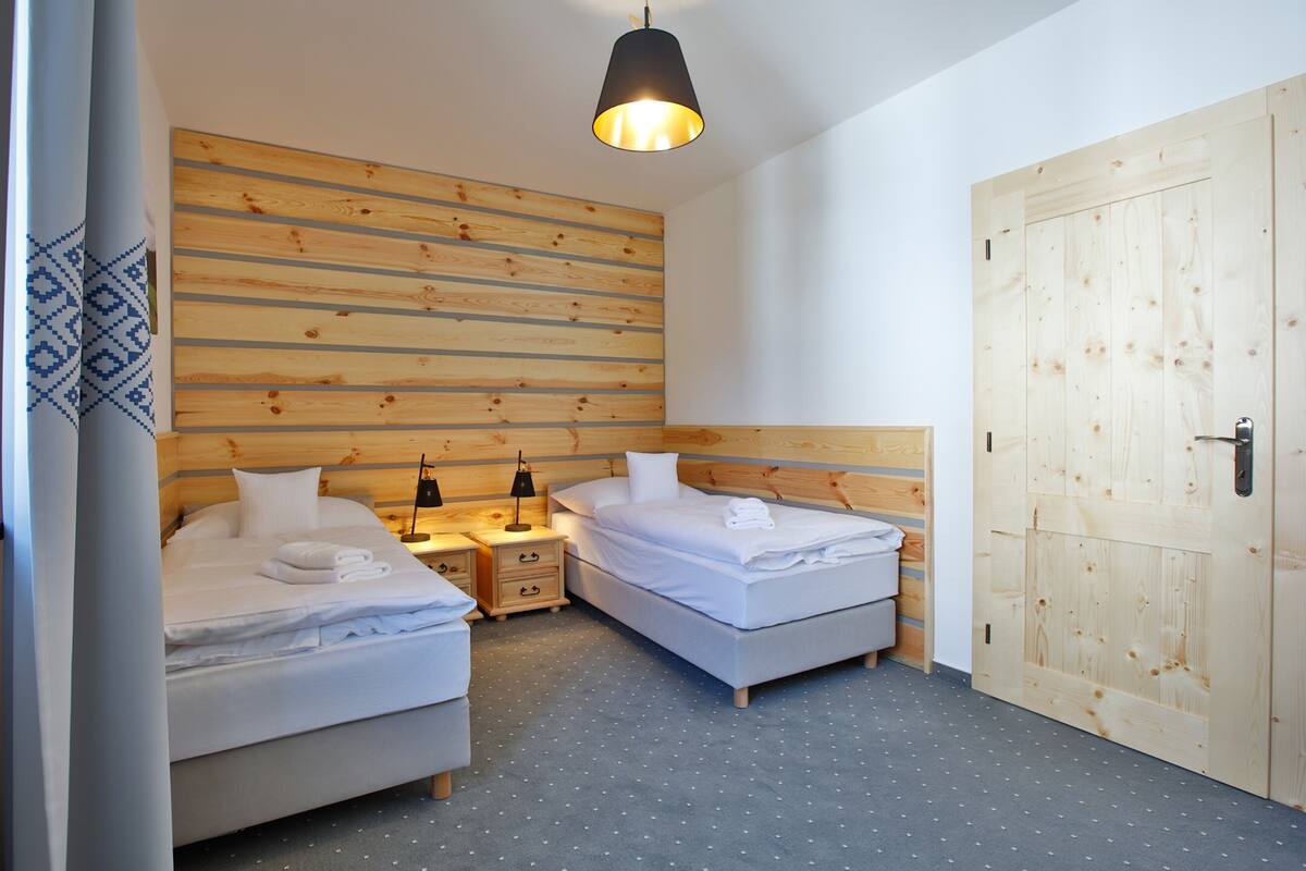Habitación de hotel con dos camas, cabecero de madera, una puerta grande de madera y una lámpara en el techo.
