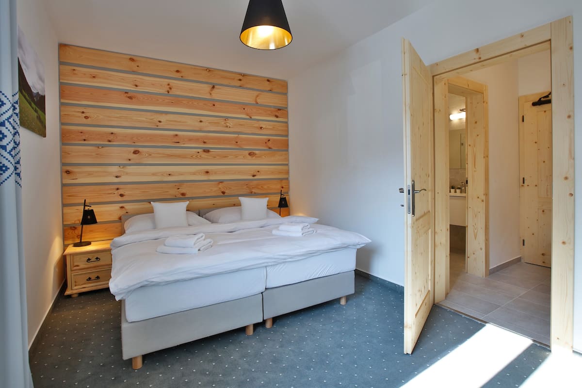 Un dormitorio con cabecera de madera, una cama doble, una mesita de noche y una puerta que da a otra habitación.