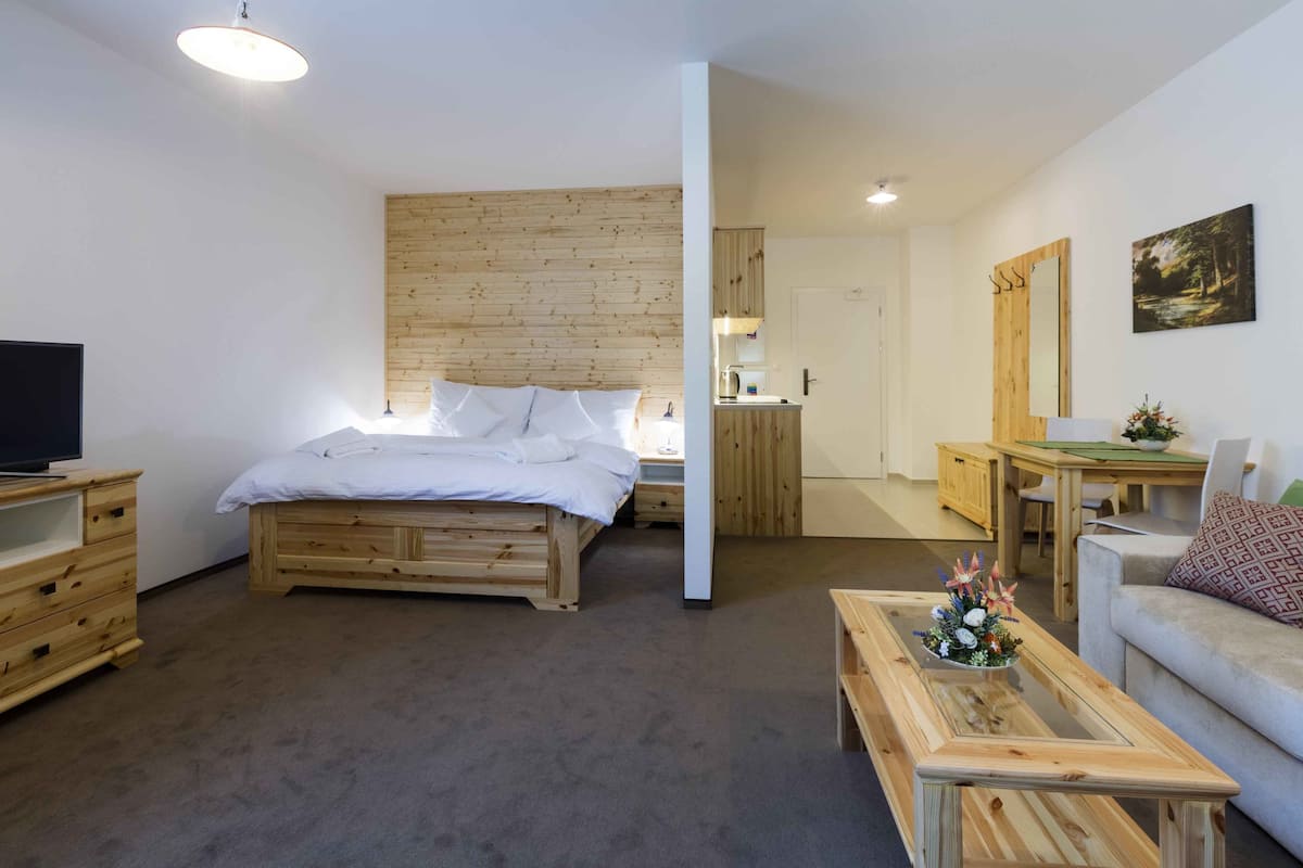 Una habitación con una cama de madera, un televisor sobre un mueble de madera, una mesita de café de madera y un sofá gris.