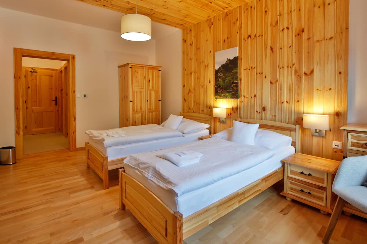 Una habitación con paneles de madera, dos camas, un armario de madera, una mesita pequeña y una silla.