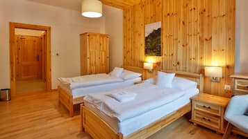 A wooden-paneled room with two beds, a wooden wardrobe, a small table, and a chair.