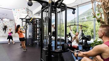 A gym with various exercise equipment, large windows, and a climbing wall.