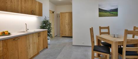 A modern kitchen with wooden cabinets, a white countertop, and a dining area with a wooden table and chairs.